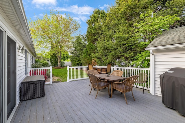 deck featuring outdoor dining area, grilling area, and view of wooded area