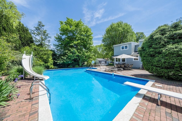 1 Karin Ct, East Northport, NY 11731 - outdoor pool featuring a water slide, a diving board, outdoor dining space, an outdoor structure, and view of wooded area