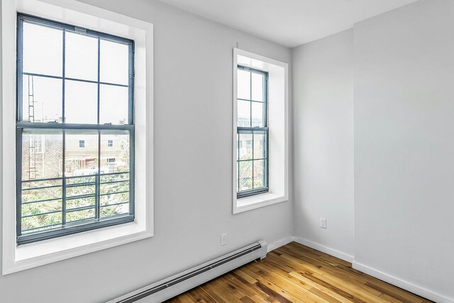 34-21 9th St, Astoria, NY 11106 - unfurnished room featuring healthy amount of natural light, a baseboard radiator, and wood finished floors
