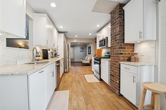 979 Manor Ln, Bay Shore, NY 11706 - kitchen with stainless steel appliances, a sink, white cabinetry, light wood-style flooring, and backsplash