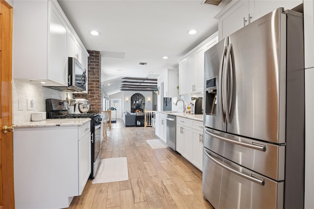 979 Manor Ln, Bay Shore, NY 11706 - kitchen with stainless steel appliances, lofted ceiling, white cabinetry, light wood-style flooring, and backsplash