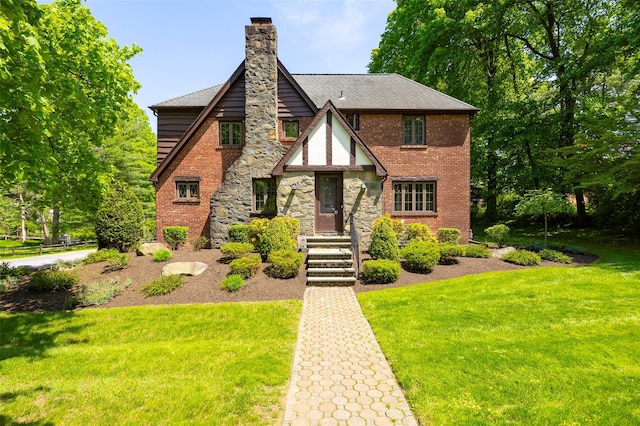 tudor house with a front yard, a chimney, stone siding, and a shingled roof