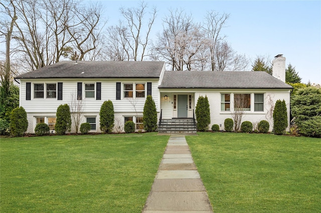tri-level home featuring a chimney, a front yard, and brick siding