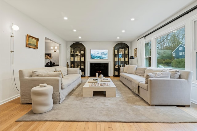 living room with hardwood / wood-style floors, recessed lighting, arched walkways, and a lit fireplace