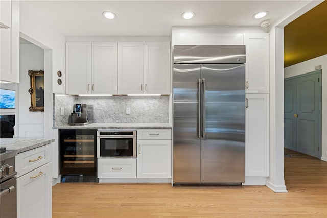 kitchen featuring appliances with stainless steel finishes, beverage cooler, white cabinets, backsplash, and light wood-style floors