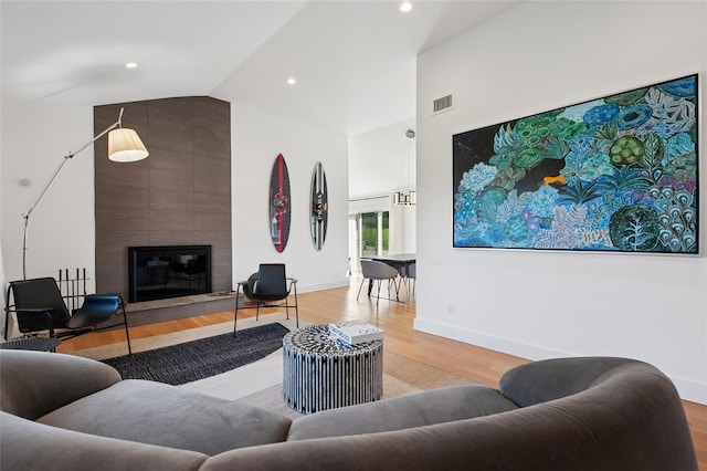 living area with wood finished floors, high vaulted ceiling, a tile fireplace, baseboards, and recessed lighting