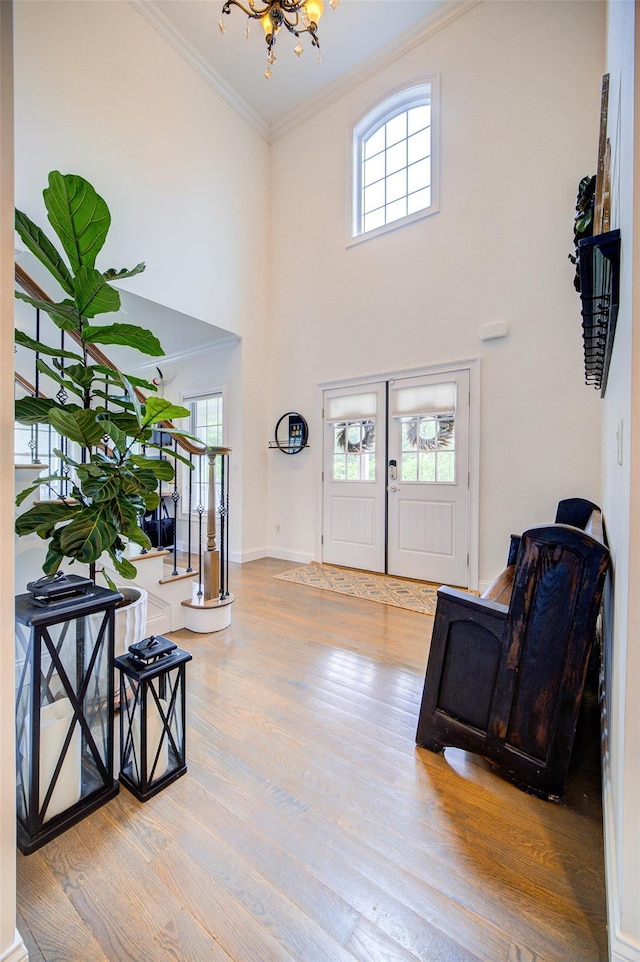 entryway featuring crown molding, a chandelier, healthy amount of natural light, wood finished floors, and a towering ceiling