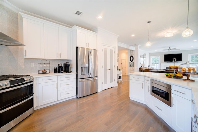 kitchen with appliances with stainless steel finishes, wall chimney exhaust hood, wood finished floors, open floor plan, and pendant lighting