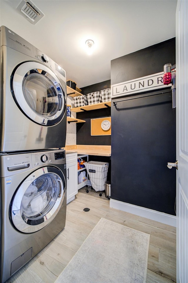 laundry area featuring estacked washer and dryer, cabinet space, and light wood-style floors