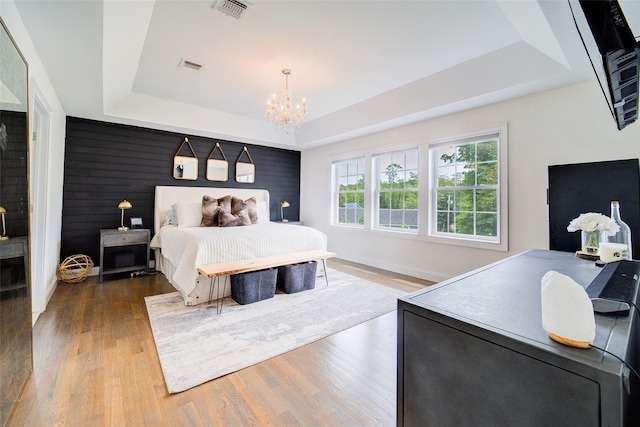bedroom with a tray ceiling, wood finished floors, a chandelier, and baseboards