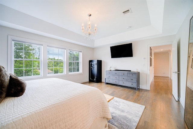 bedroom featuring a chandelier, a tray ceiling, light wood-style flooring, and baseboards