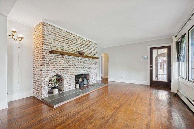 2600 Garden St, Baldwin, NY 11510 - unfurnished living room featuring baseboard heating, arched walkways, wood finished floors, baseboards, and crown molding
