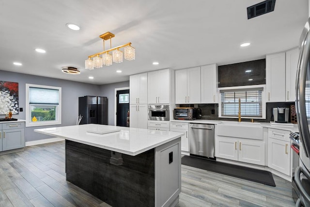 181 Central Park Rd E, Plainview, NY 11803 - kitchen featuring appliances with stainless steel finishes, tasteful backsplash, a center island, white cabinetry, and wood finished floors