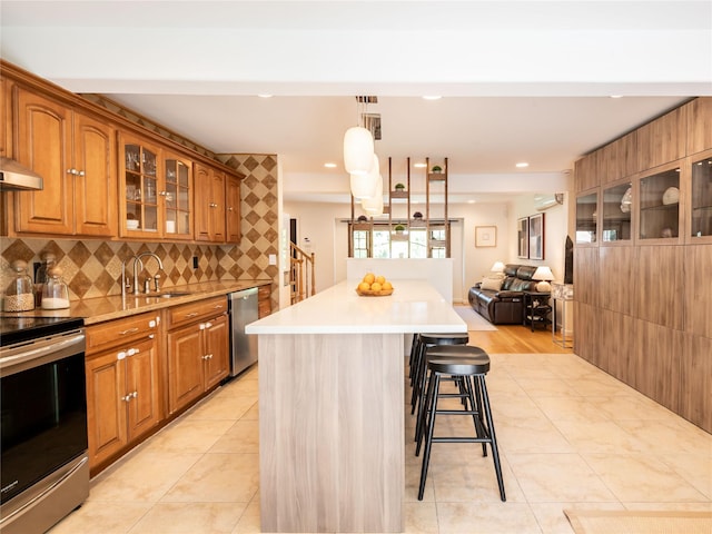 94 Shadyside Ave, Port Washington, NY 11050 - kitchen featuring appliances with stainless steel finishes, a sink, brown cabinetry, a breakfast bar, and glass insert cabinets