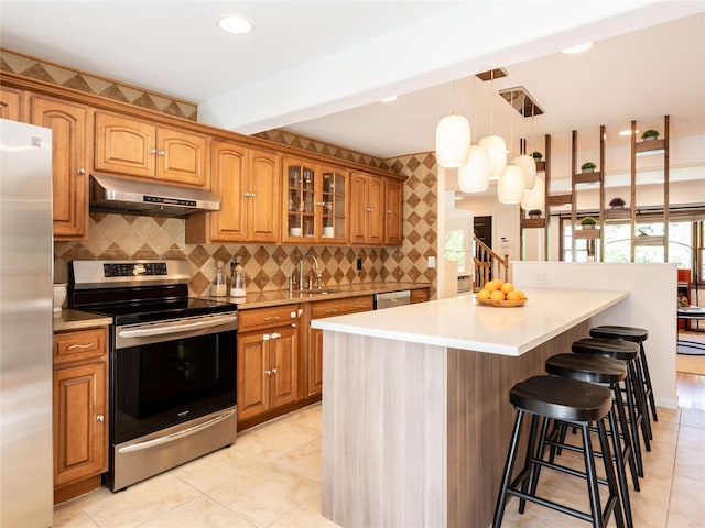 94 Shadyside Ave, Port Washington, NY 11050 - kitchen featuring stainless steel appliances, under cabinet range hood, a breakfast bar, brown cabinetry, and recessed lighting