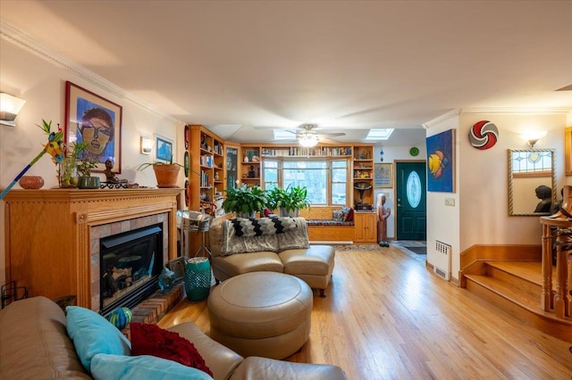 living area with light wood-style flooring, a fireplace, a ceiling fan, ornamental molding, and built in features