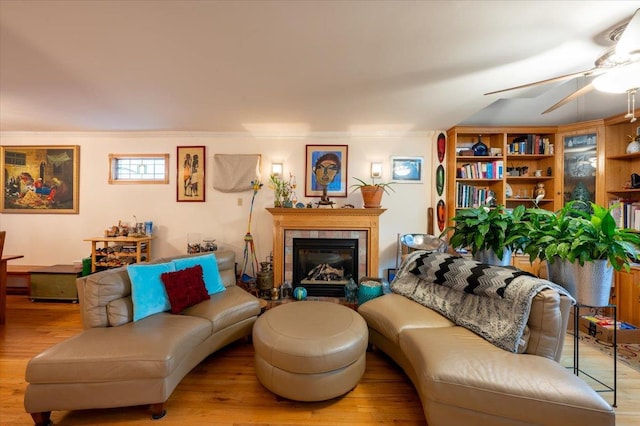 living room featuring wood finished floors, a ceiling fan, a tile fireplace, and crown molding