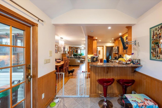 indoor dry bar with wainscoting, stainless steel microwave, wood walls, lofted ceiling, and a chandelier