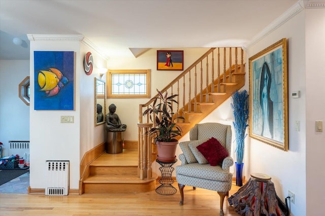 stairs featuring radiator heating unit, wood finished floors, crown molding, and baseboards