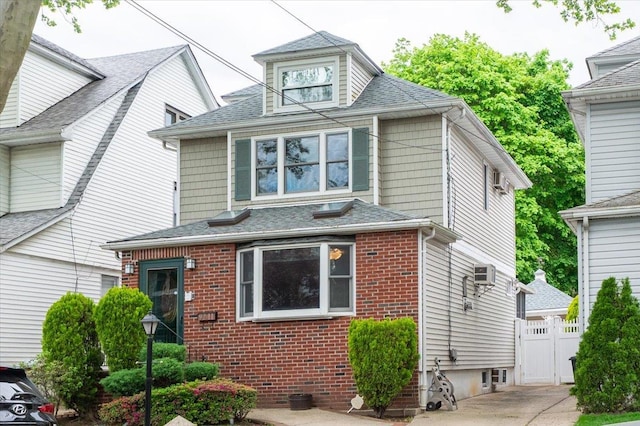 traditional style home featuring brick siding, fence, roof with shingles, and an AC wall unit