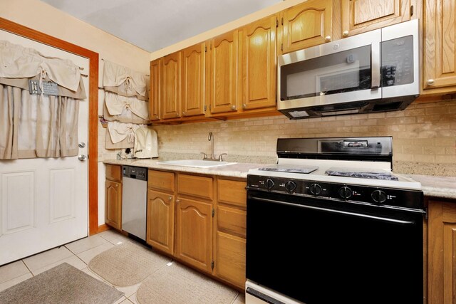 kitchen with appliances with stainless steel finishes, a sink, light countertops, backsplash, and light tile patterned floors