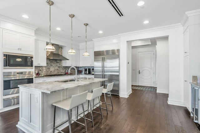kitchen with built in appliances, wall chimney range hood, a sink, a warming drawer, and baseboards