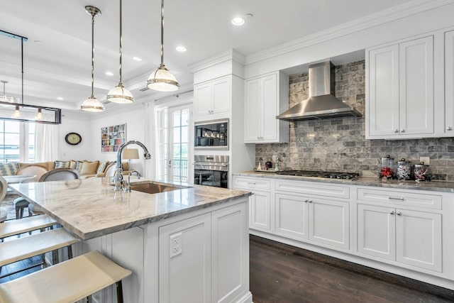 kitchen with wall chimney exhaust hood, appliances with stainless steel finishes, a sink, ornamental molding, and dark wood-style floors