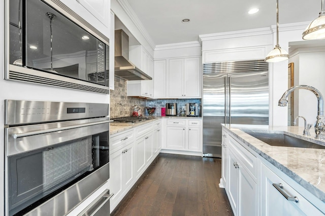 kitchen with built in appliances, a sink, wall chimney range hood, crown molding, and decorative backsplash