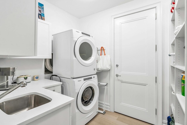 clothes washing area with stacked washing machine and dryer, cabinet space, and light wood-style flooring
