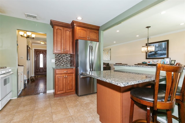 kitchen with freestanding refrigerator, a chandelier, white gas stove, a breakfast bar area, and backsplash