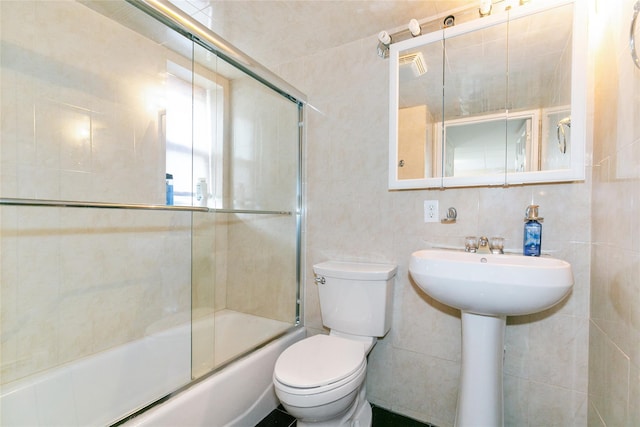 full bathroom with toilet, bath / shower combo with glass door, a sink, and tile walls