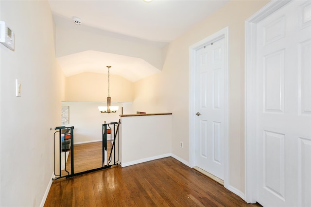hallway with an upstairs landing, a chandelier, dark wood finished floors, baseboards, and vaulted ceiling