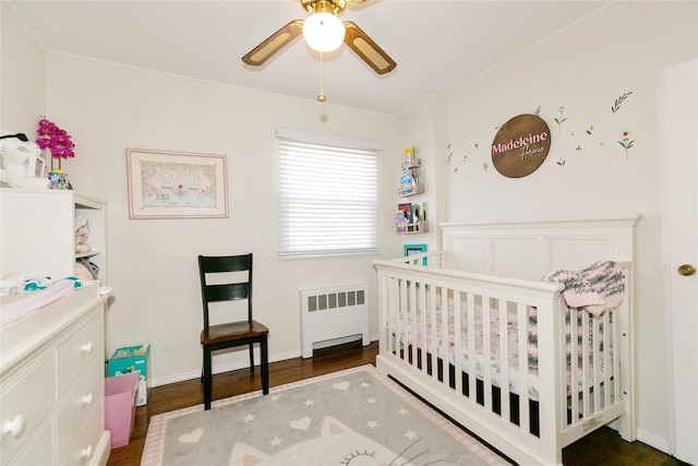 bedroom with radiator, a crib, wood finished floors, and a ceiling fan