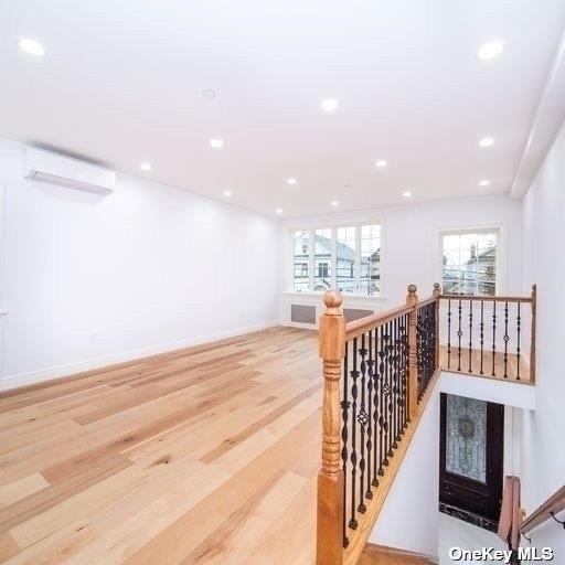 corridor with a wall unit AC, an upstairs landing, light wood-style flooring, recessed lighting, and baseboards