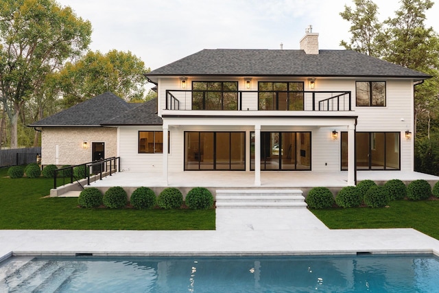 rear view of house featuring a balcony, a patio, a chimney, and a shingled roof