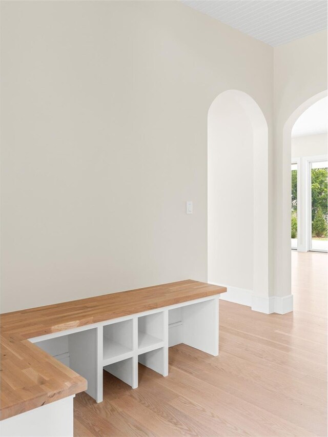 mudroom featuring arched walkways, light wood-style floors, and baseboards