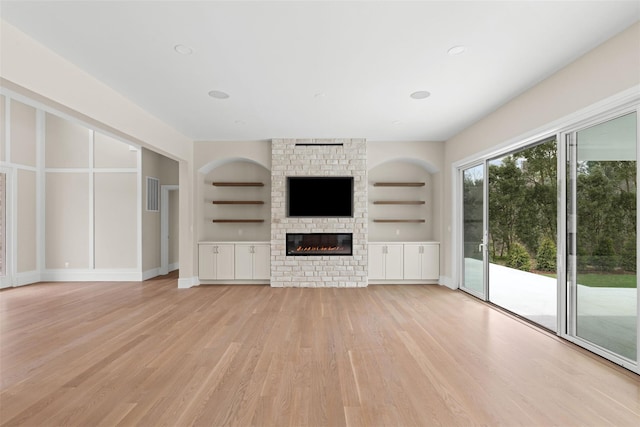 unfurnished living room featuring light wood-style flooring, built in features, a large fireplace, and baseboards
