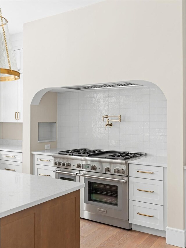 kitchen featuring double oven range, white cabinets, light stone counters, tasteful backsplash, and light wood-style floors
