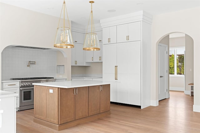 kitchen with stainless steel range, arched walkways, light countertops, and a kitchen island