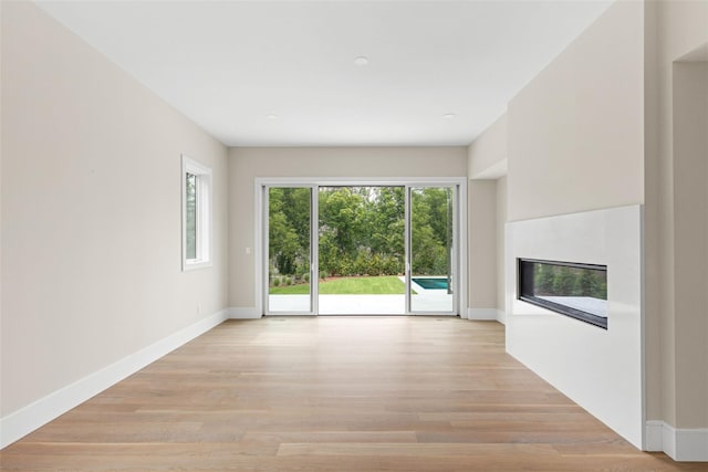 unfurnished living room featuring healthy amount of natural light, a glass covered fireplace, light wood finished floors, and baseboards