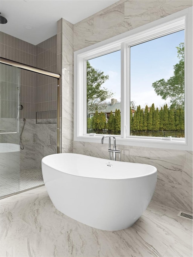 bathroom featuring a stall shower, healthy amount of natural light, a freestanding tub, and tile walls