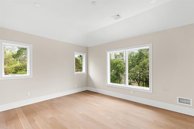 spare room with healthy amount of natural light, light wood-style floors, baseboards, and vaulted ceiling