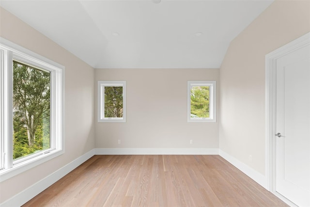 unfurnished room with plenty of natural light, lofted ceiling, light wood finished floors, and baseboards