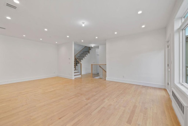 empty room featuring light wood-style floors, radiator heating unit, recessed lighting, baseboards, and stairs