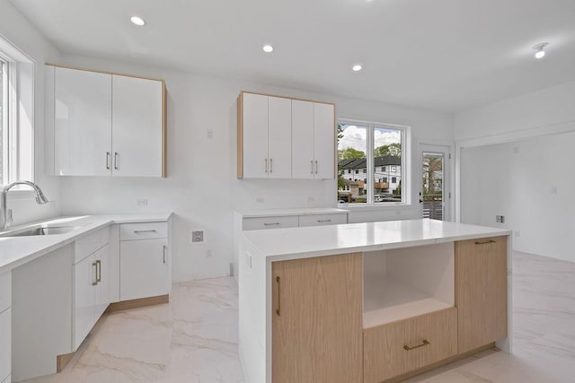 kitchen with a sink, light marble finish floors, recessed lighting, light countertops, and white cabinetry