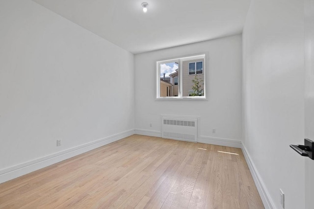 unfurnished room with radiator heating unit, light wood-type flooring, and baseboards