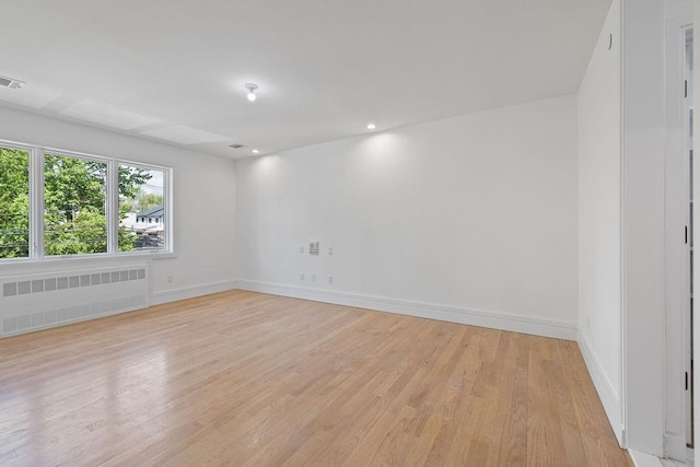 unfurnished room featuring radiator heating unit, light wood-type flooring, and baseboards