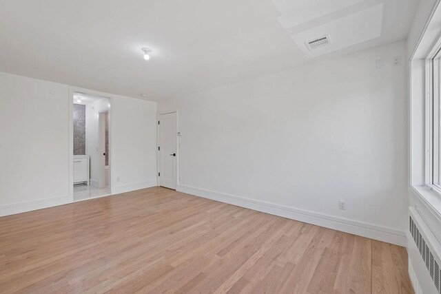 spare room with radiator heating unit, light wood-type flooring, and baseboards