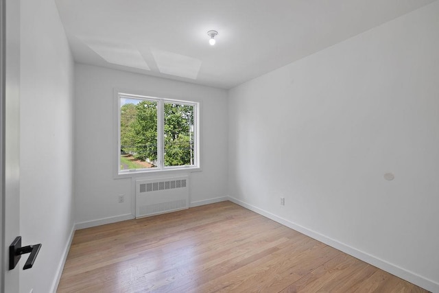 spare room featuring radiator, light wood-style floors, and baseboards