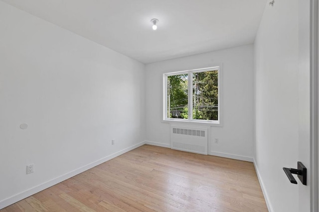 unfurnished room with radiator, light wood-style flooring, and baseboards